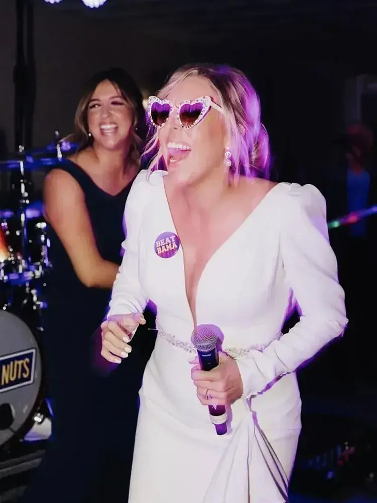 Magnolia Valley Weddings & Events woman in a white suit sings into a microphone during the reception.