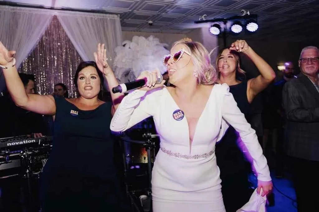 A woman in a white dress and sunglasses dances with friends at Magnolia Valley Weddings & Events.